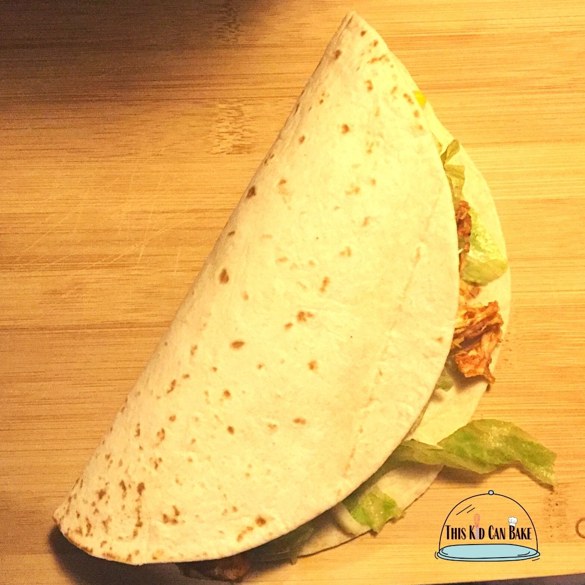 A picture of shredded chicken inside a folded tortilla with lettuce and tomato.
