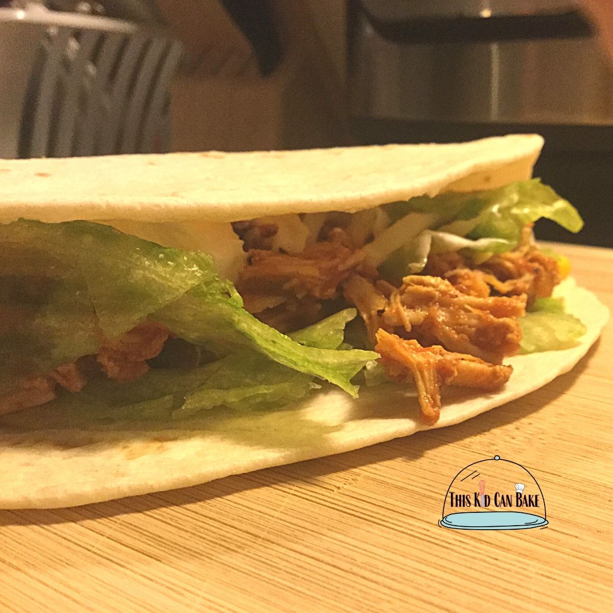 A picture of shredded chicken on a tortilla with lettuce and tomato.