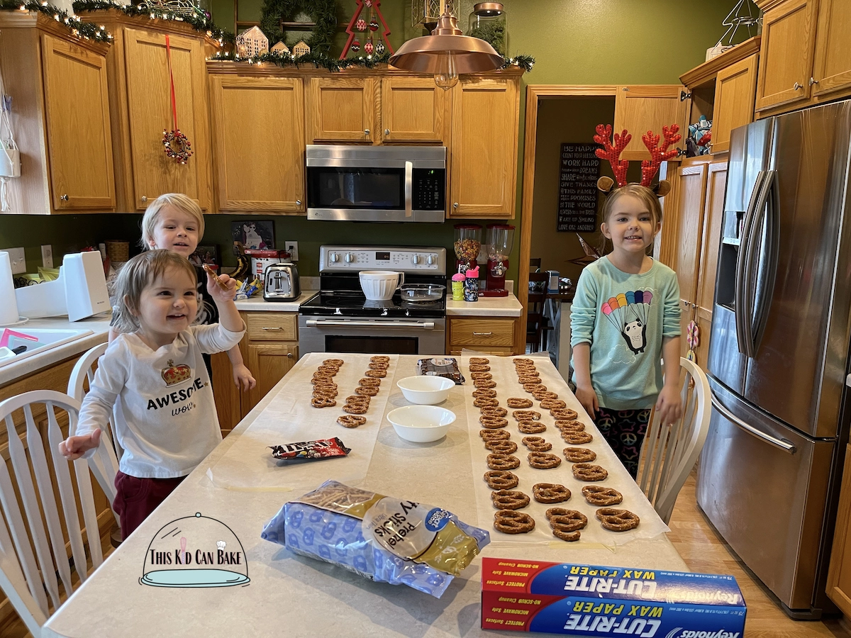 A picture of three kids preparing their workspace in the kitchen to make chocolate reindeer pretzels